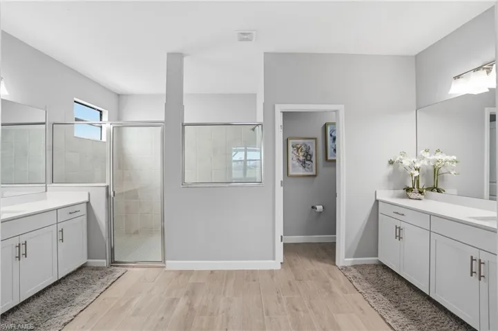 Bathroom featuring two vanities, wood finish floors, and a stall shower