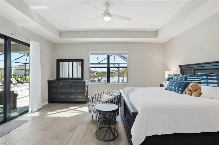 Bedroom featuring access to exterior, a water view, wood finished floors, ceiling fan, and a tray ceiling