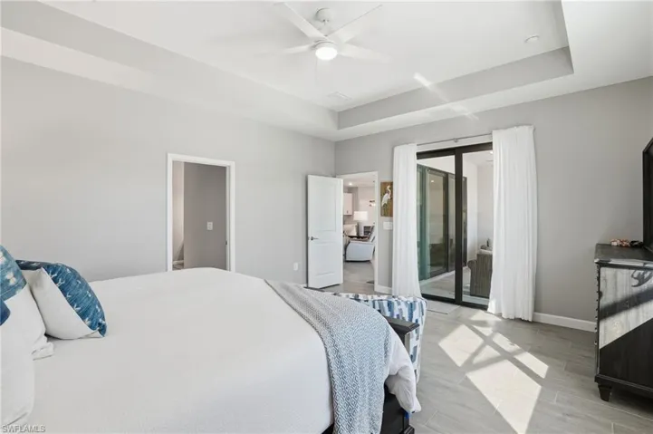 Bedroom with a raised ceiling, access to exterior, wood finish floors, and ceiling fan