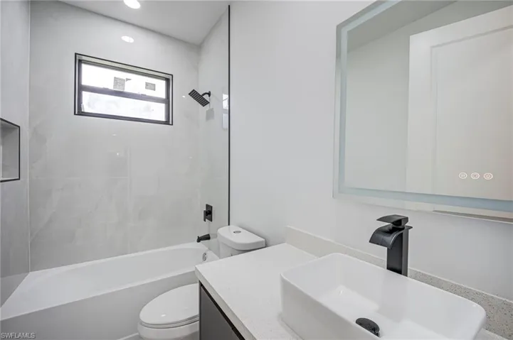 Sleek bathroom featuring a vessel sink, dark cabinetry, an illuminated mirror, and a tub with a built-in niche