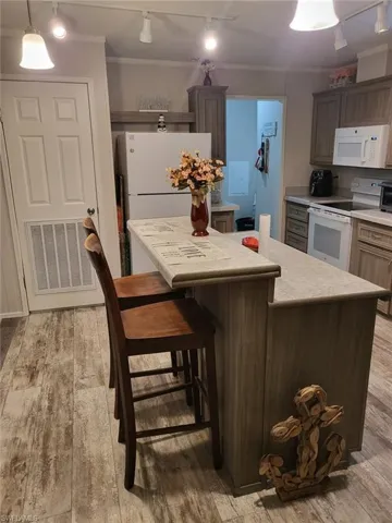 Kitchen with rail lighting, crown molding, light countertops, a center island, and white appliances