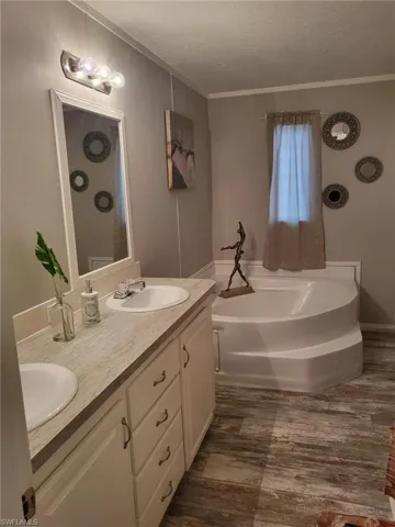 Bathroom with double vanity, a garden tub, a textured ceiling, dark wood-type flooring, and crown molding