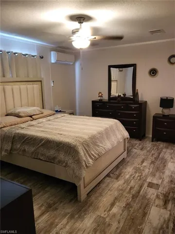 Bedroom with hardwood / wood-style floors, ceiling fan, a wall unit AC, and a textured ceiling