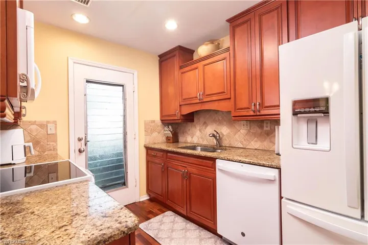Kitchen with white appliances, light stone countertops, brown cabinets, and tasteful backsplash