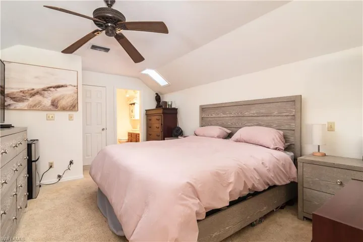 Bedroom featuring vaulted ceiling, carpet, ensuite bath, and ceiling fan