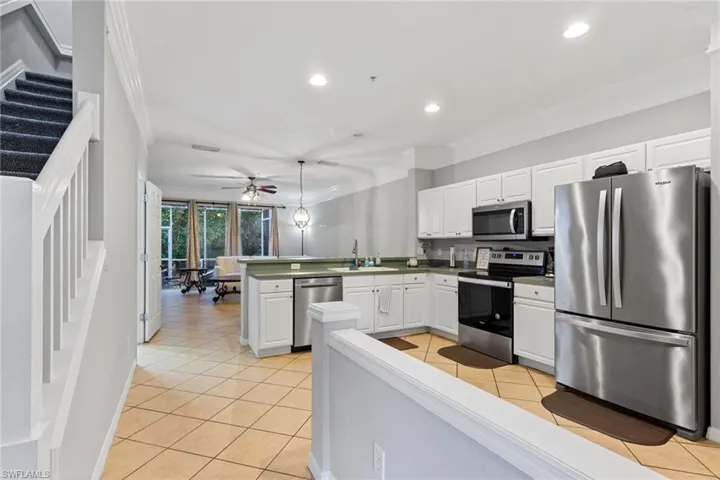 Kitchen with kitchen peninsula, ceiling fan, appliances with stainless steel finishes, white cabinetry, and ornamental molding
