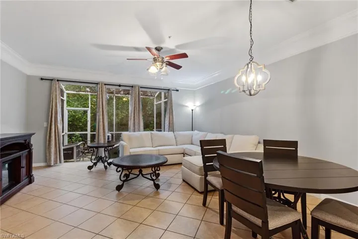 Living room with crown molding, light tile patterned flooring, and ceiling fan with notable chandelier