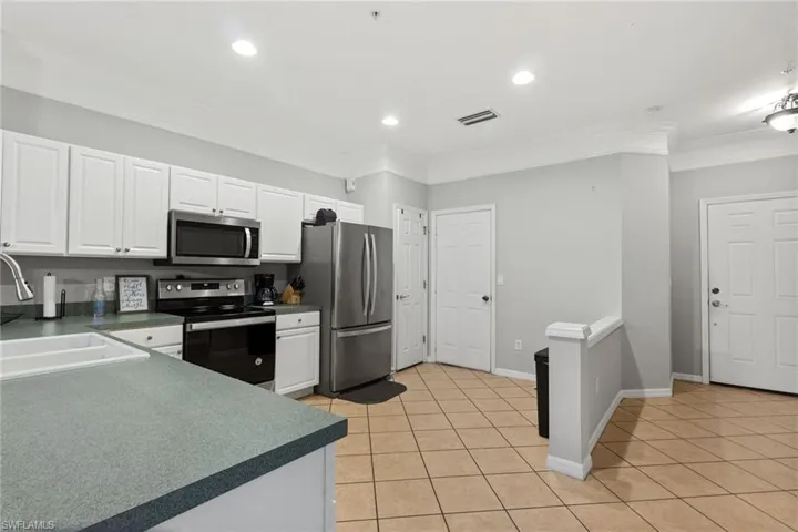 Kitchen featuring white cabinets, light tile patterned floors, ornamental molding, sink, and stainless steel appliances