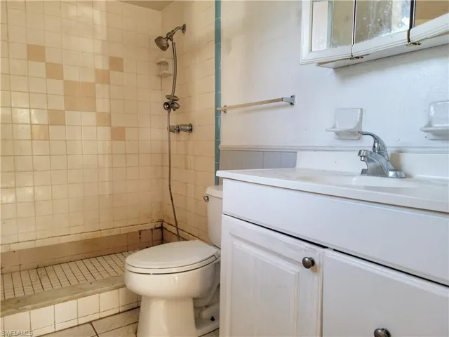 Bathroom with tiled shower, vanity, and toilet