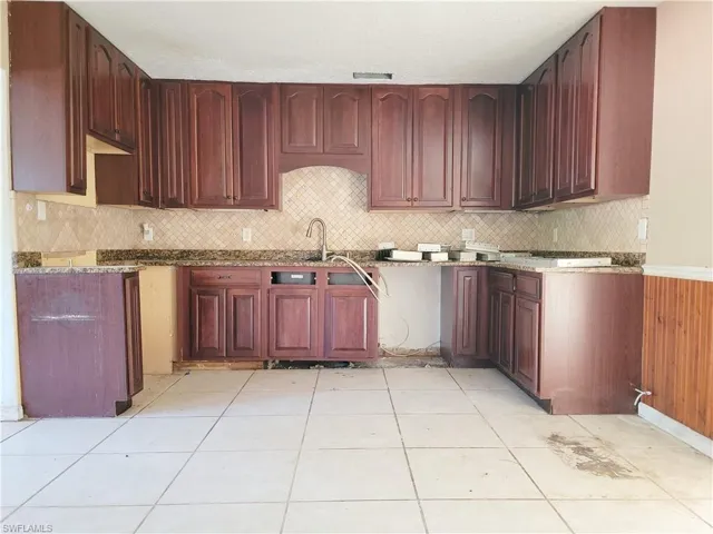 Kitchen featuring light tile patterned floors, stone counters, a sink, dark brown cabinets, and backsplash