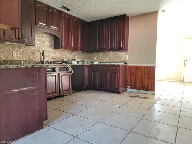 Kitchen with a textured ceiling, light tile patterned floors, dark brown cabinets, decorative backsplash, and dark stone counters