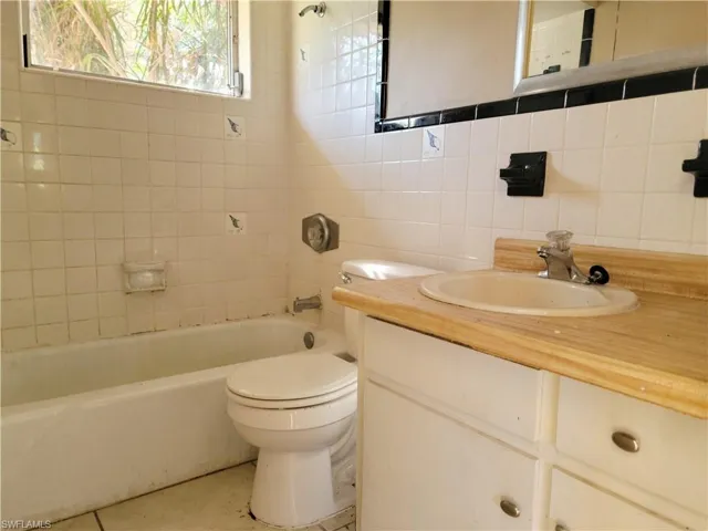 Bathroom with tasteful backsplash, toilet, tile patterned flooring, vanity, and tile walls