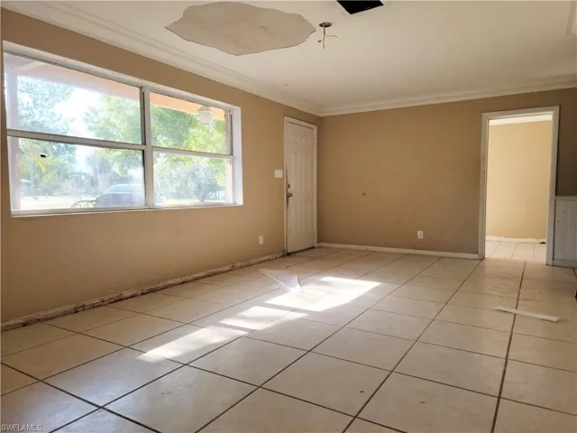 Empty room featuring ornamental molding, light tile patterned flooring, and baseboards