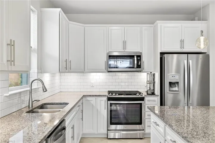 Kitchen featuring appliances with stainless steel finishes, light stone countertops, and white cabinetry
