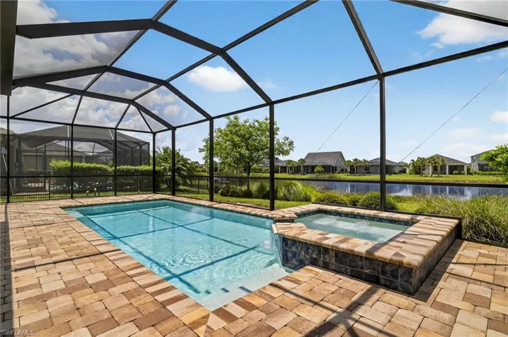 View of pool featuring a water view, a patio area, a pool with connected hot tub, and glass enclosure
