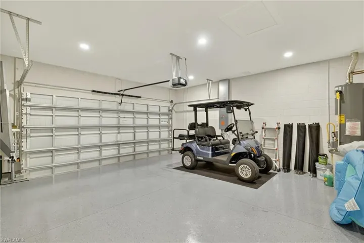 Garage with a garage door opener, gas water heater, concrete block wall, and recessed lighting