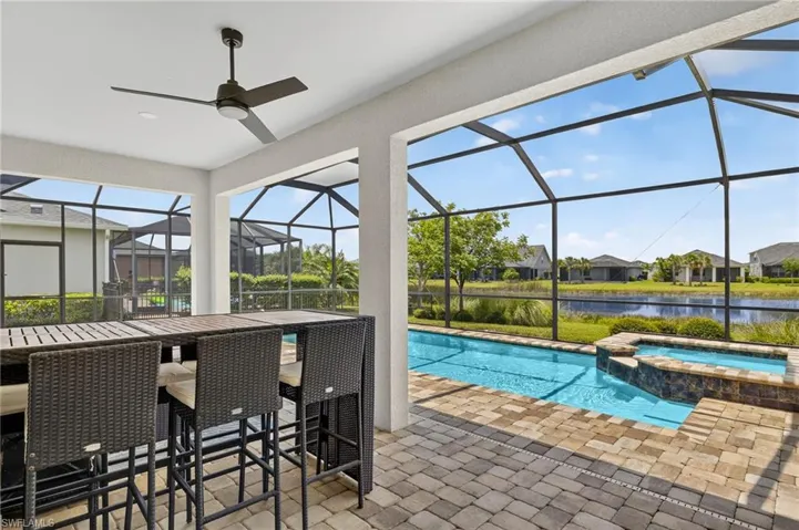 View of pool featuring a water view, a patio area, a pool with connected hot tub, and glass enclosure