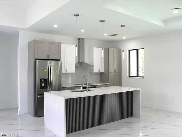 Modern kitchen featuring a waterfall island with ribbed detailing, stainless steel appliances, a range hood, pendant lighting, and recessed ceiling lights