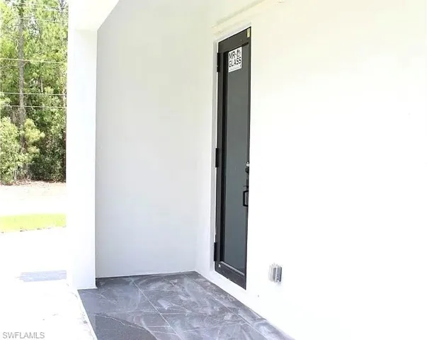 Modern exterior entry with a dark-framed glass panel door, white stucco siding, and large format gray tile flooring