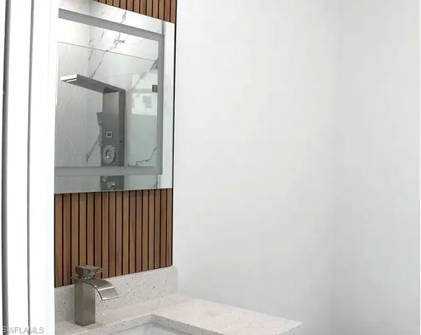 Modern vanity featuring a square vessel sink, brushed nickel waterfall faucet, and light-toned composite countertop