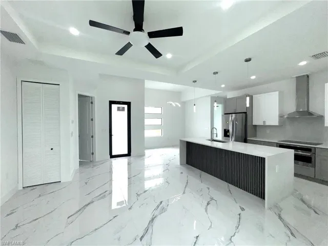 Open-concept kitchen and living area featuring high ceilings, recessed lighting, and large format white tile flooring with gray veining