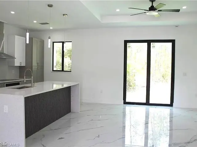 Open-concept living area featuring large format marble-look flooring, a kitchen island with stone countertops and a fluted panel base, recessed lighting, and a modern ceiling fan