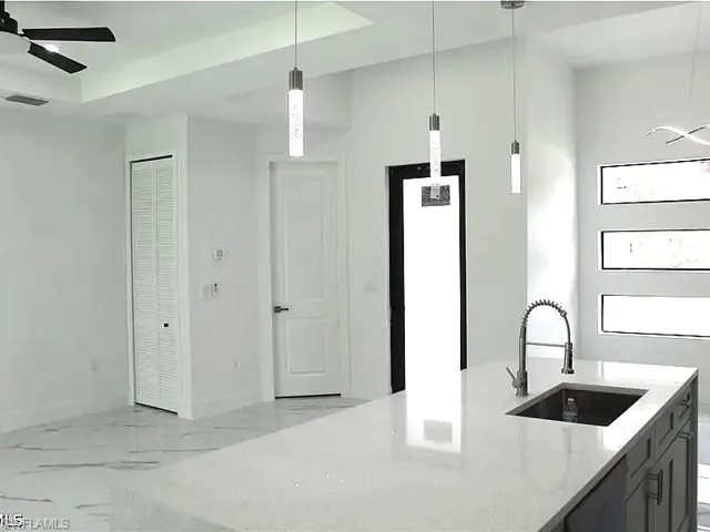 Kitchen island featuring a single-basin sink with a gooseneck faucet, light-toned countertop, and dark cabinetry