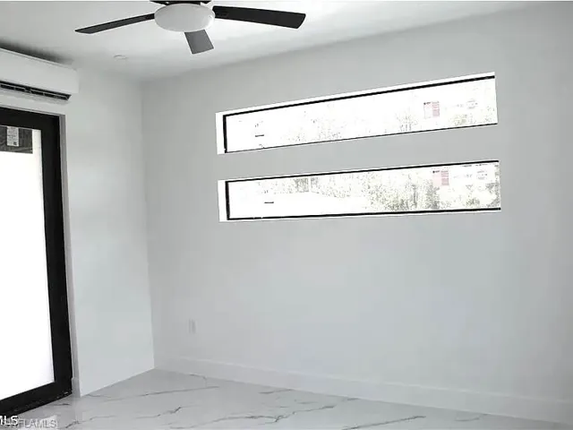 Bright interior space featuring two horizontal transom windows, a large black-framed door, a ceiling fan with integrated lighting, and a wall-mounted air conditioning unit