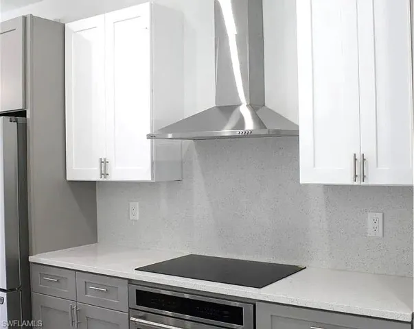 Modern kitchen featuring white upper cabinetry, gray lower cabinetry, a stainless steel range hood, an integrated cooktop, and a light-toned speckled countertop