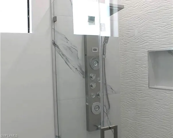 Glass-enclosed shower featuring a multi-function shower panel with integrated handheld spray and rain shower head