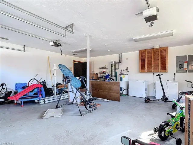 Garage featuring refrigerator, electric panel, a garage door opener, and electric water heater