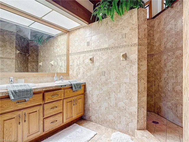 Full bathroom featuring a skylight, a walk in shower, tile walls, and vanity