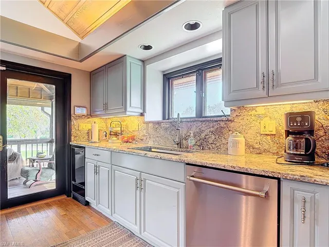 Kitchen featuring a sink, stainless steel dishwasher, decorative backsplash, light stone countertops, and light wood finished floors
