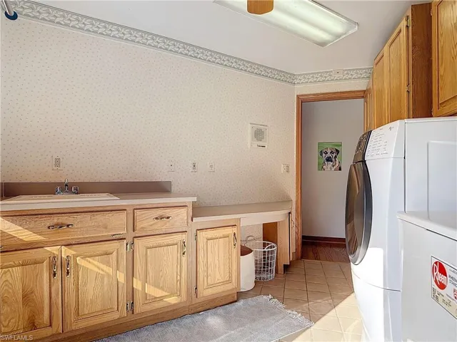 Laundry area with washing machine and clothes dryer, light tile patterned floors, cabinet space, a sink, and wallpapered walls