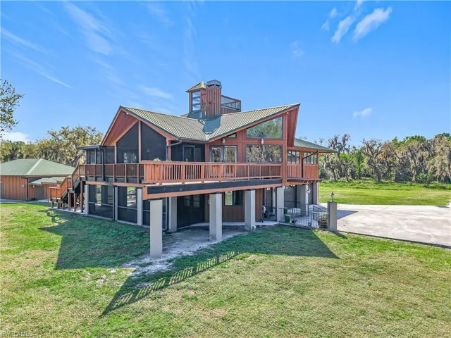 Back of property featuring metal roof, a sunroom, stairs, concrete driveway, and a lawn