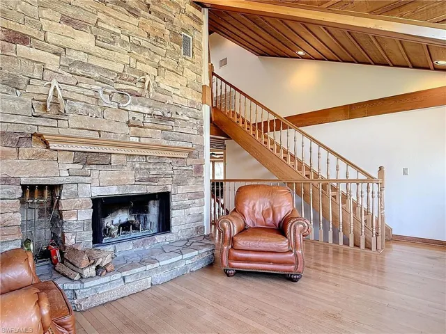 Living room featuring wood ceiling, wood finished floors, vaulted ceiling with beams, stairs, and a fireplace