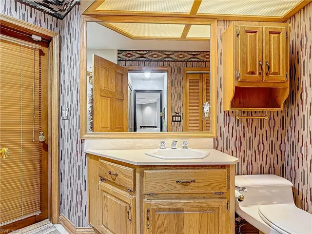 Bathroom with toilet, wallpapered walls, and vanity