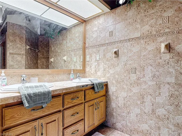Full bath featuring double vanity, tiled shower, a sink, and tile walls