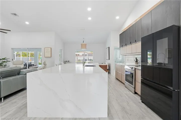 Kitchen featuring open floor plan, freestanding refrigerator, stainless steel range with electric stovetop, recessed lighting, and light stone counters