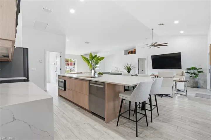 Two tone kitchen with light stone countertops, a large island, open floor plan, a breakfast bar area, and light wood-style flooring