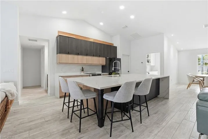 Kitchen with light stone countertops, a breakfast bar area, a large island, lofted ceiling, and light wood-type flooring