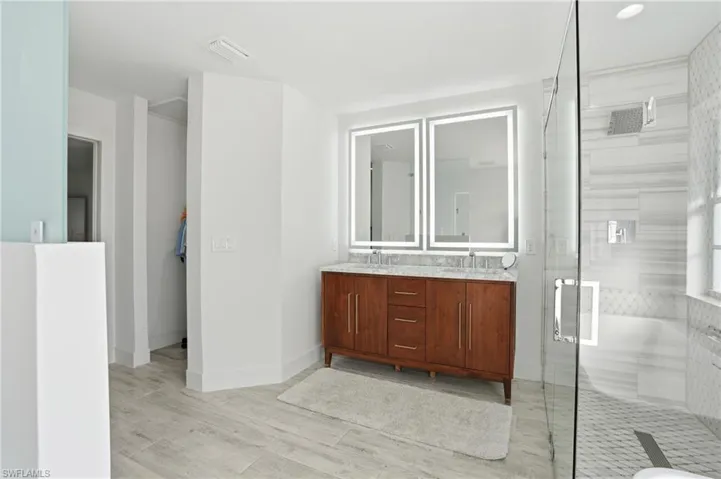 Full bath with double vanity, a shower stall, and light wood finished floors
