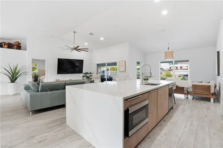 Kitchen featuring open floor plan, a center island with sink, light stone counters, vaulted ceiling, and light wood-type flooring