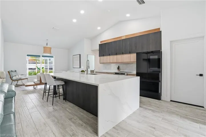 Two tone kitchen featuring light stone countertops, vaulted ceiling, dual tone cabinets, light wood-style floors, and freestanding refrigerator