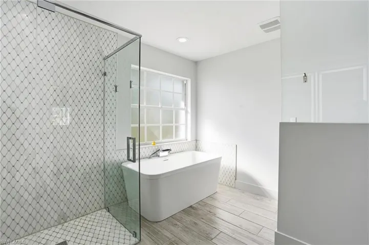 Bathroom featuring wood tiled floors, a stall shower, a freestanding bath, and recessed lighting