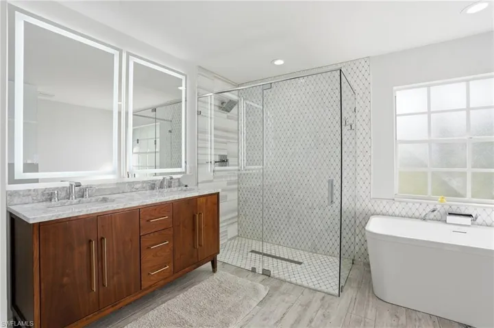 Bathroom featuring a stall shower, double vanity, a soaking tub, light wood finished floors, and tile walls