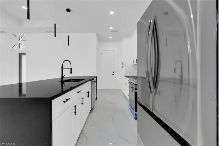 Kitchen featuring freestanding refrigerator, white cabinetry, a kitchen island with sink, dark stone counters, and recessed lighting