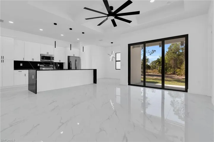 Kitchen featuring open floor plan, a kitchen island with sink, white cabinetry, appliances with stainless steel finishes, and a tray ceiling