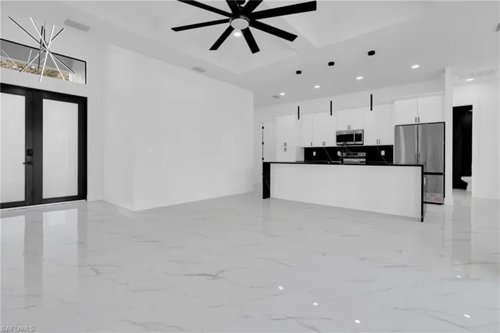 Kitchen with open floor plan, hanging light fixtures, coffered ceiling, stainless steel appliances, and white cabinetry