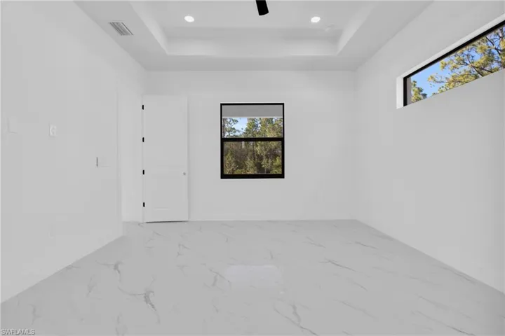 Unfurnished room with a raised ceiling, light marble finish floors, recessed lighting, and a ceiling fan